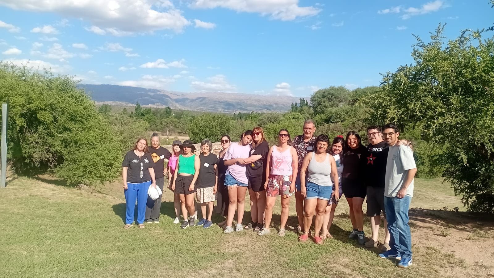 Grupo de viajeras y viajeros de pie sobre el pasto, con las sierras de Córdoba de fondo, en Villa Cura Brochero.